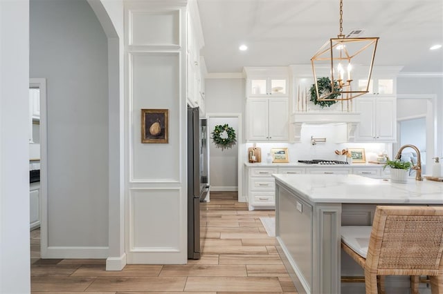 kitchen featuring arched walkways, wood finish floors, gas stovetop, glass insert cabinets, and a sink