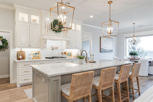 kitchen with stainless steel gas cooktop, tasteful backsplash, light wood finished floors, and crown molding