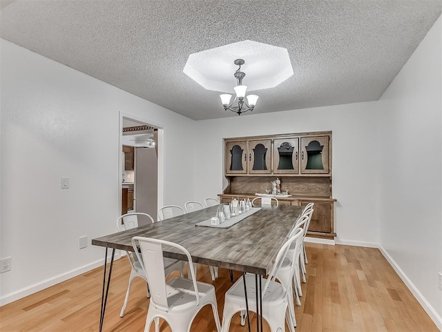 dining room featuring a raised ceiling, a chandelier, light hardwood / wood-style floors, and a textured ceiling