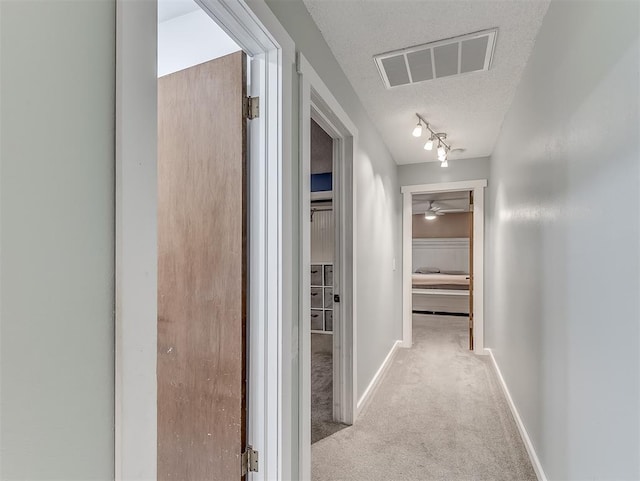 hall featuring light colored carpet, rail lighting, and a textured ceiling