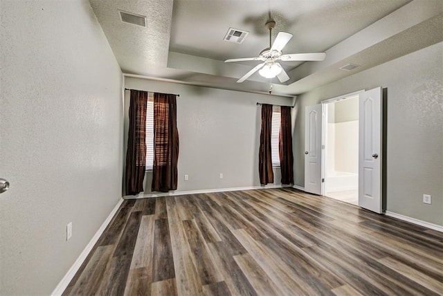 unfurnished bedroom with dark wood-type flooring, ceiling fan, connected bathroom, and a tray ceiling