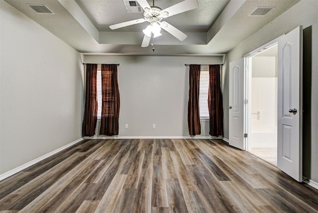 unfurnished bedroom with ceiling fan, wood-type flooring, a tray ceiling, and connected bathroom