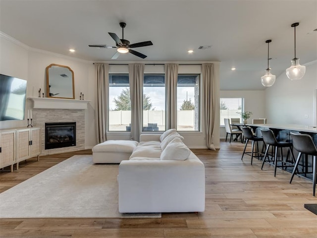 living room featuring a fireplace, light hardwood / wood-style flooring, ornamental molding, and ceiling fan