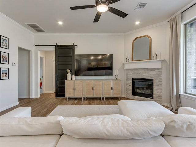 living room featuring crown molding, light hardwood / wood-style floors, a barn door, and ceiling fan