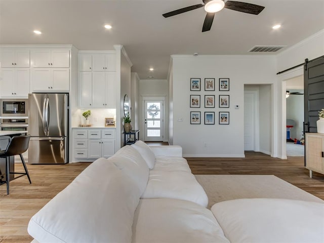 living room featuring ceiling fan, ornamental molding, a barn door, and light hardwood / wood-style floors