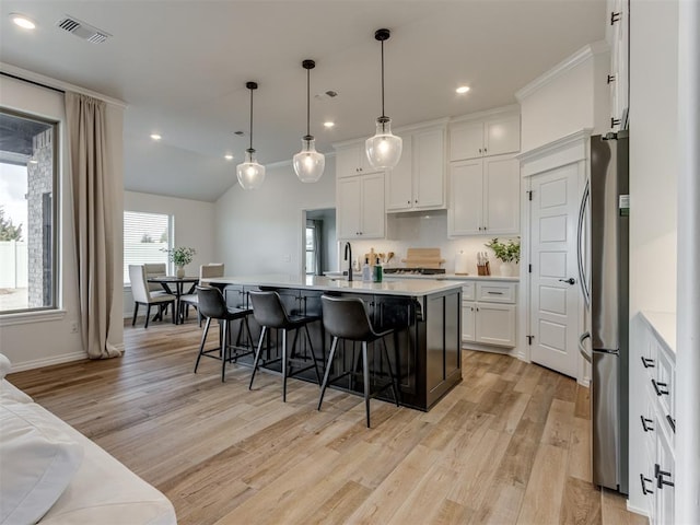 kitchen featuring stainless steel fridge, white cabinets, hanging light fixtures, a kitchen island with sink, and light wood-type flooring