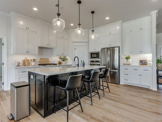 kitchen with white cabinetry, pendant lighting, stainless steel appliances, and an island with sink