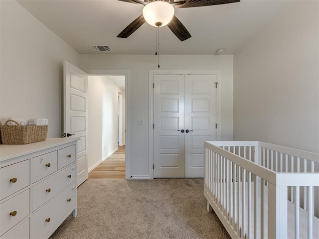 bedroom with light carpet, a crib, a closet, and ceiling fan