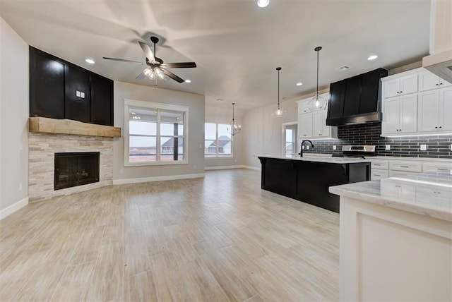 kitchen featuring ceiling fan with notable chandelier, a tile fireplace, white cabinets, decorative backsplash, and stainless steel electric stove