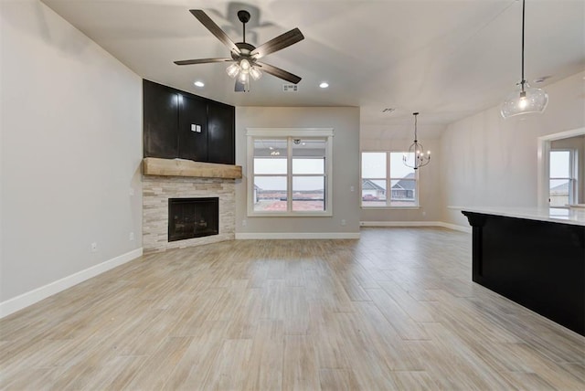 unfurnished living room featuring ceiling fan with notable chandelier, a wealth of natural light, and light hardwood / wood-style flooring