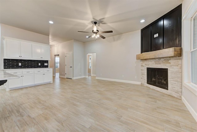 unfurnished living room with a stone fireplace, light hardwood / wood-style flooring, and ceiling fan