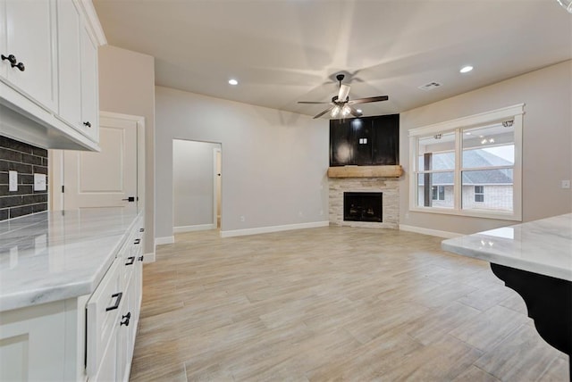 living room with a stone fireplace, ceiling fan, and light hardwood / wood-style flooring