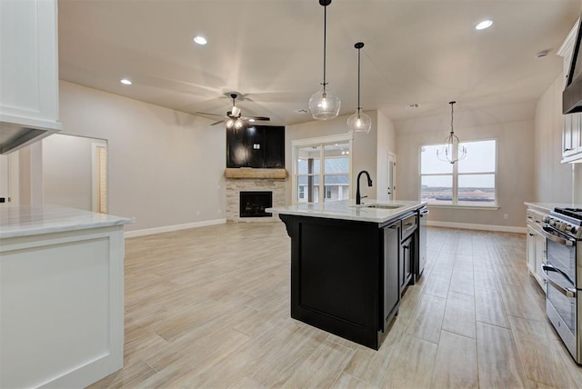 kitchen featuring a stone fireplace, sink, decorative light fixtures, appliances with stainless steel finishes, and a kitchen island with sink