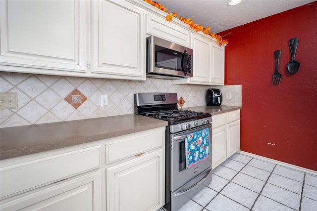 kitchen featuring stainless steel appliances, tasteful backsplash, light tile patterned floors, and white cabinets