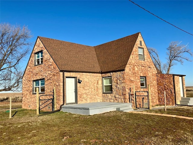 back of house featuring stone siding, roof with shingles, and a lawn