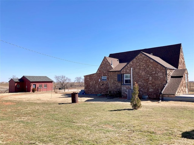 view of home's exterior featuring stone siding, a lawn, and central air condition unit