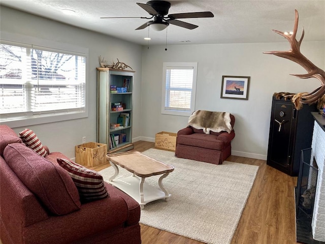 living room featuring light wood-style flooring, a fireplace, baseboards, and ceiling fan