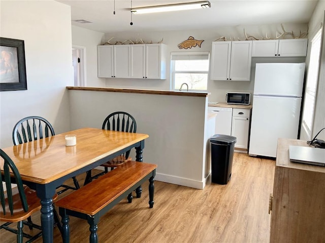 kitchen featuring white appliances, a sink, white cabinets, light countertops, and light wood-type flooring