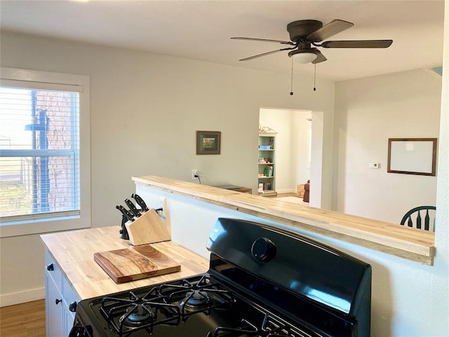 kitchen featuring butcher block countertops, ceiling fan, black gas range oven, and wood finished floors