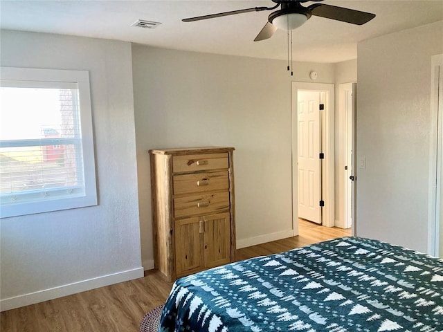 bedroom featuring a ceiling fan, wood finished floors, visible vents, and baseboards