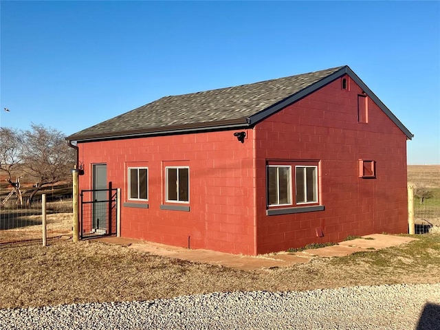 view of property exterior featuring a shingled roof, an outbuilding, and concrete block siding