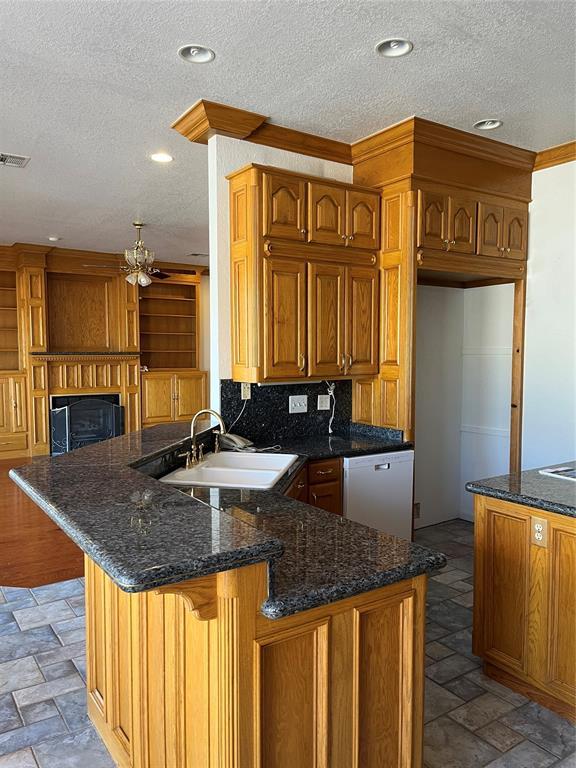 kitchen with sink, a textured ceiling, dishwasher, kitchen peninsula, and dark stone counters