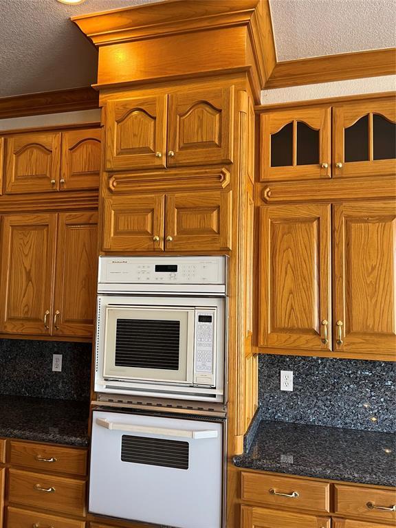 kitchen with tasteful backsplash, a textured ceiling, double oven, and dark stone counters