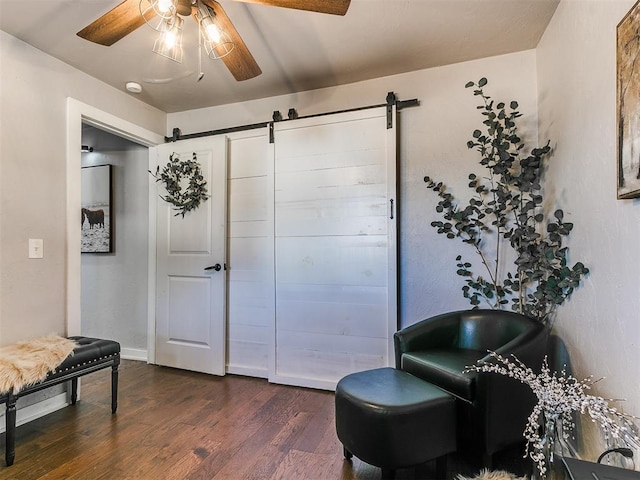 sitting room with dark hardwood / wood-style floors, a barn door, and ceiling fan