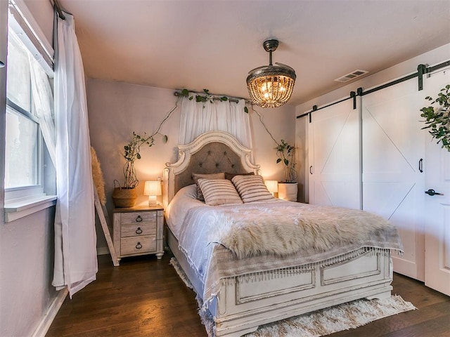 bedroom featuring a barn door, an inviting chandelier, and dark hardwood / wood-style flooring