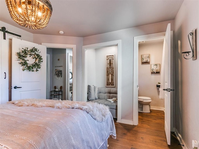 bedroom with connected bathroom, a notable chandelier, dark wood-type flooring, and a barn door