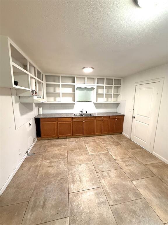 kitchen featuring brown cabinetry, a sink, a textured ceiling, and open shelves