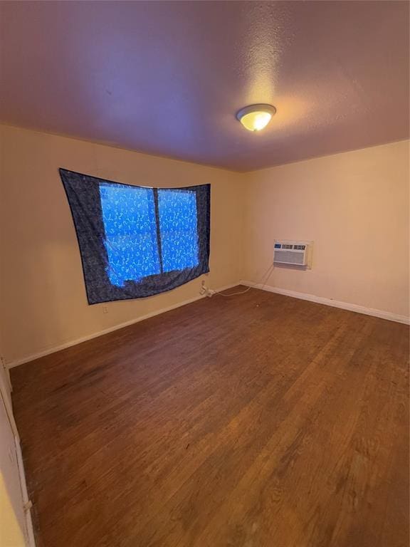 empty room featuring dark wood-style floors, a wall mounted AC, a textured ceiling, and baseboards