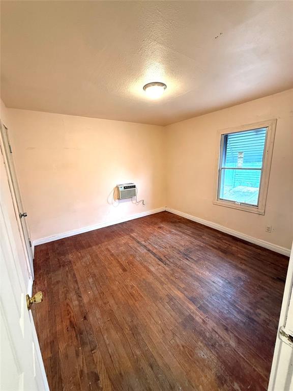 empty room with dark wood-style floors, baseboards, a textured ceiling, and a wall mounted AC