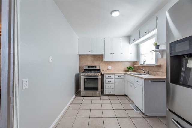 kitchen with sink, tasteful backsplash, light tile patterned floors, stainless steel range with gas stovetop, and white cabinets