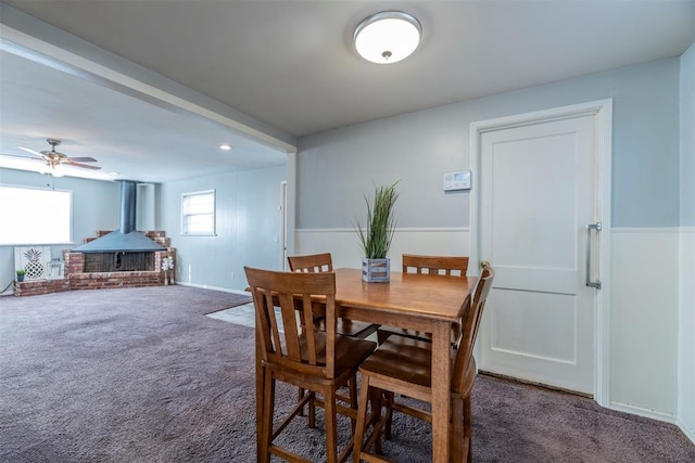 carpeted dining space with beam ceiling, ceiling fan, and a wood stove