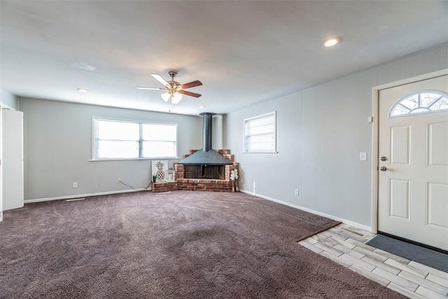 foyer entrance with a wood stove, light colored carpet, and ceiling fan