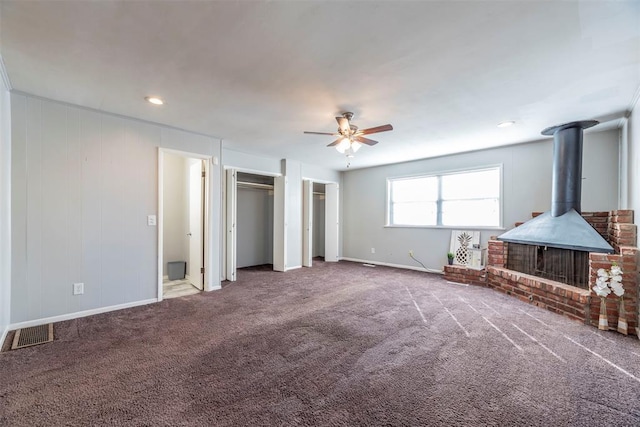 unfurnished living room with a wood stove, ceiling fan, and carpet flooring