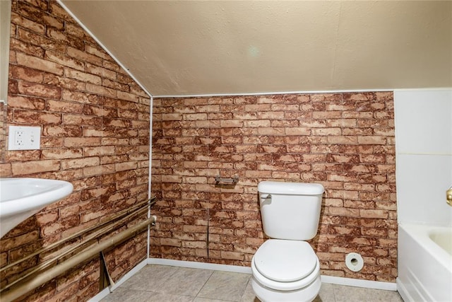 bathroom featuring brick wall, lofted ceiling, a textured ceiling, and toilet