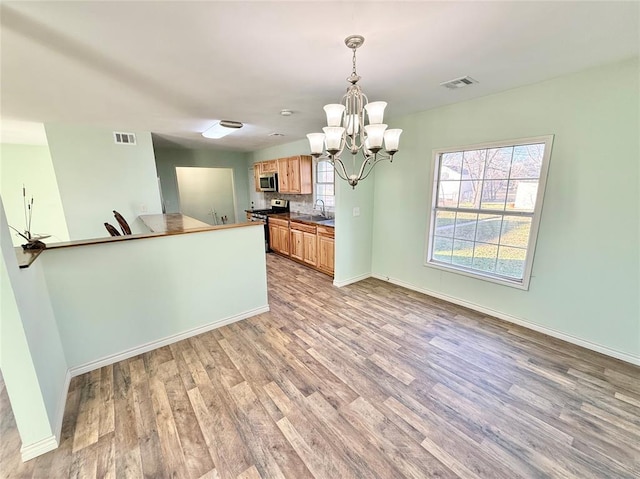 kitchen with decorative light fixtures, sink, a chandelier, stainless steel appliances, and light hardwood / wood-style flooring