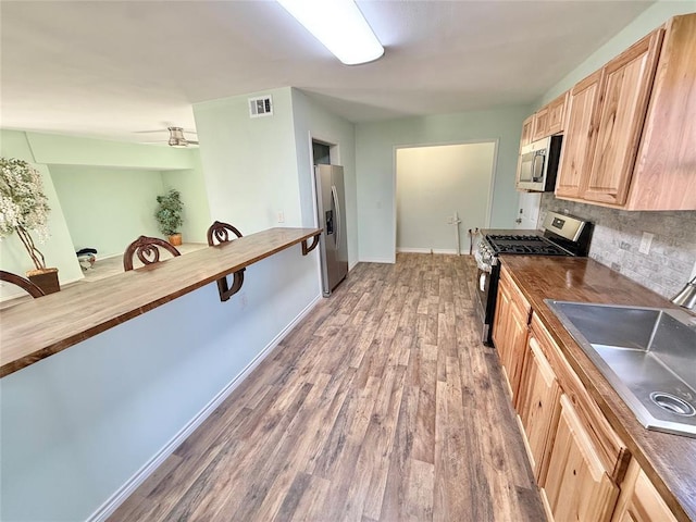 kitchen featuring sink, backsplash, stainless steel appliances, wood-type flooring, and light brown cabinets