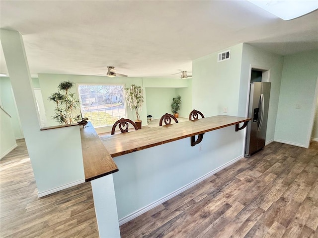 kitchen with wooden counters, stainless steel refrigerator with ice dispenser, wood-type flooring, a kitchen bar, and kitchen peninsula