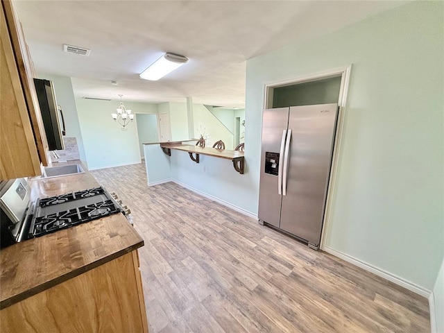 kitchen with pendant lighting, stainless steel fridge, a chandelier, light hardwood / wood-style floors, and kitchen peninsula