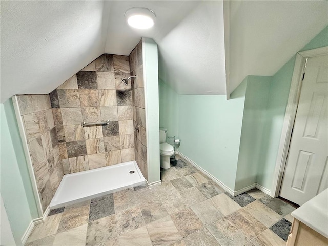 bathroom with tiled shower, lofted ceiling, toilet, and a textured ceiling