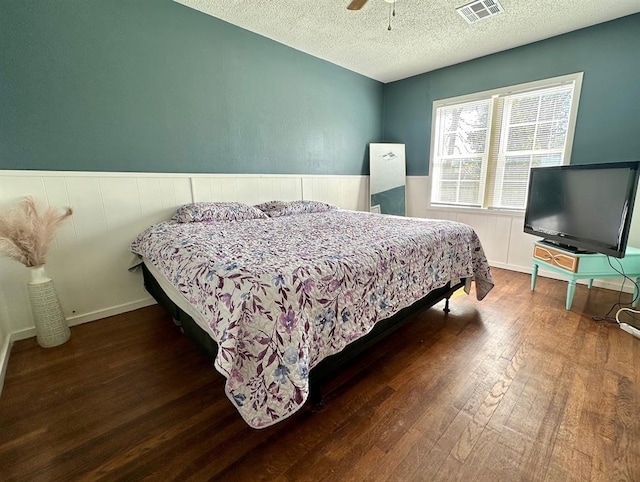 bedroom with visible vents, a textured ceiling, hardwood / wood-style floors, wainscoting, and ceiling fan