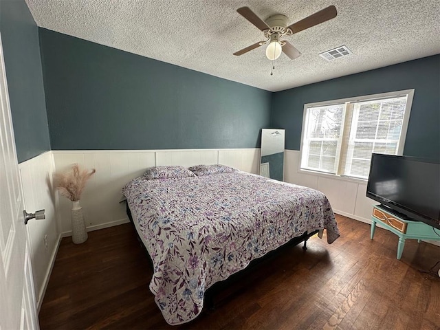 bedroom featuring visible vents, a wainscoted wall, hardwood / wood-style floors, a textured ceiling, and a ceiling fan