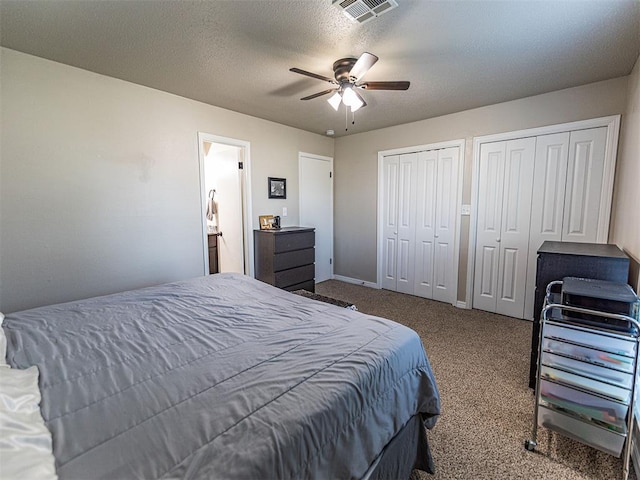 bedroom featuring ceiling fan, a textured ceiling, carpet, and two closets