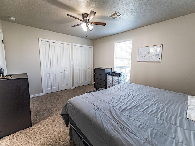 carpeted bedroom featuring multiple closets, ceiling fan, and a textured ceiling