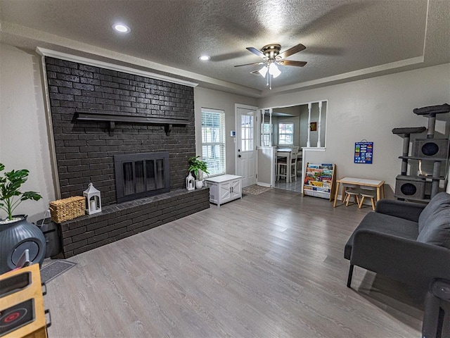 living room with a textured ceiling, a tray ceiling, ceiling fan, a fireplace, and hardwood / wood-style floors