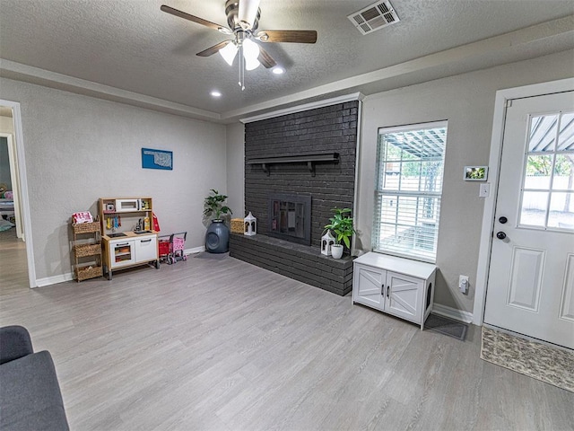 living room featuring ceiling fan, a fireplace, a textured ceiling, and light hardwood / wood-style flooring