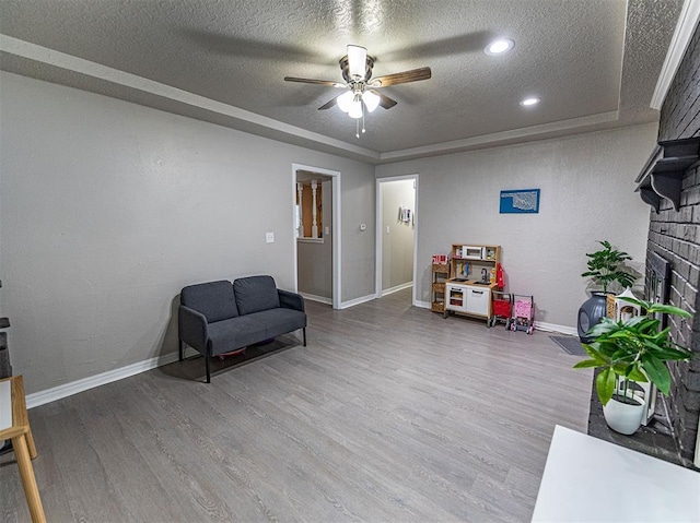 sitting room featuring hardwood / wood-style flooring, ceiling fan, a textured ceiling, a brick fireplace, and a raised ceiling